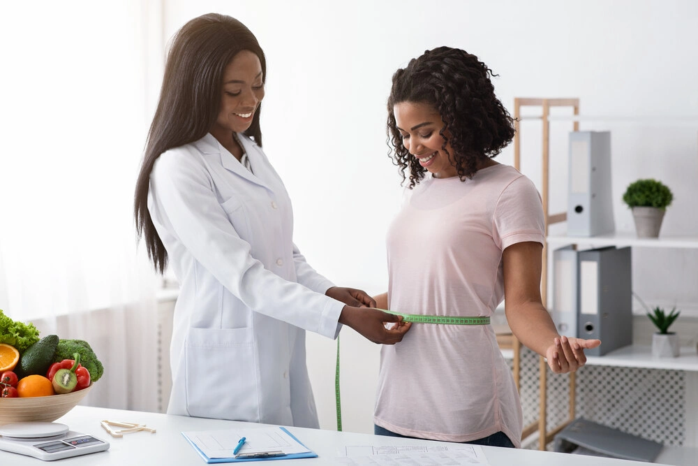 Young black woman taking body measurements at dietologist, clinic interior