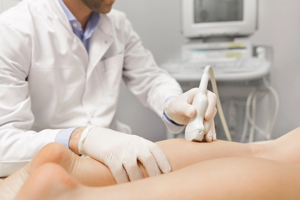 Orthopedist doctor doing ultrasound examination of patient's leg veins in his office
