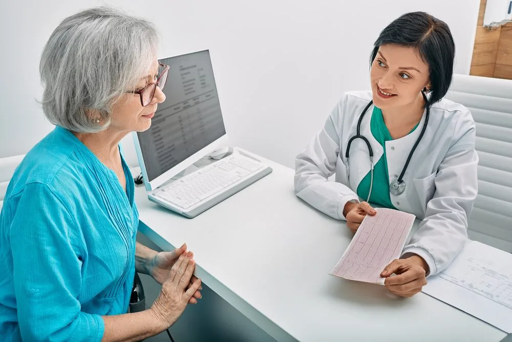 Positive doctor consulting senior woman on results of cardiogram and test