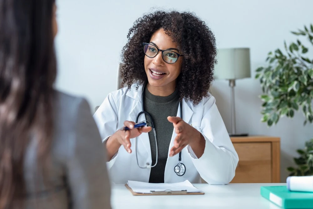 Shot of beautiful cheerful female doctor talking while explaining medical treatment to patient in the consultation.