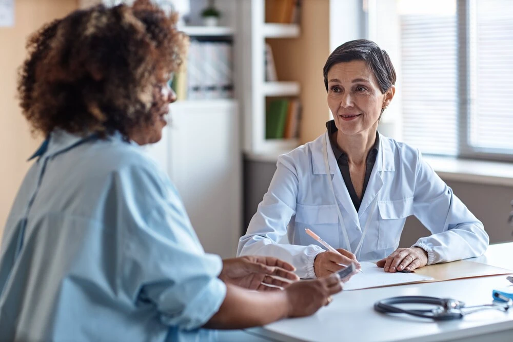 Medium shot of smiling doctor consulting African American female patient while sitting in clinic office