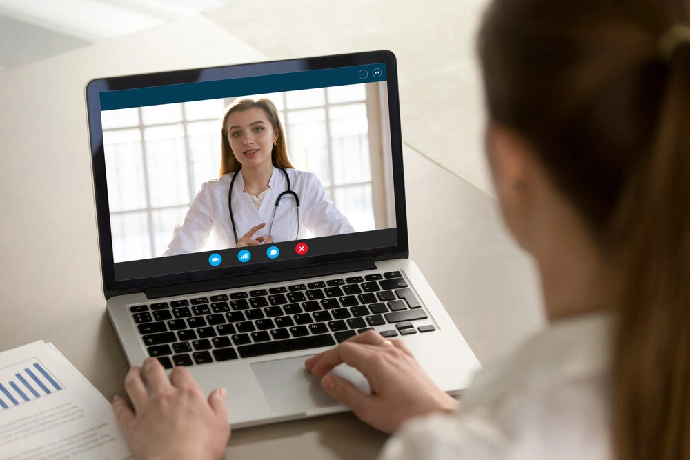 Shoulder view young woman consulting with family therapist doctor general practitioner online via video call on laptop