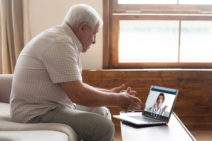 Elderly man sit on couch at home have online consultation on computer with female doctor or physician